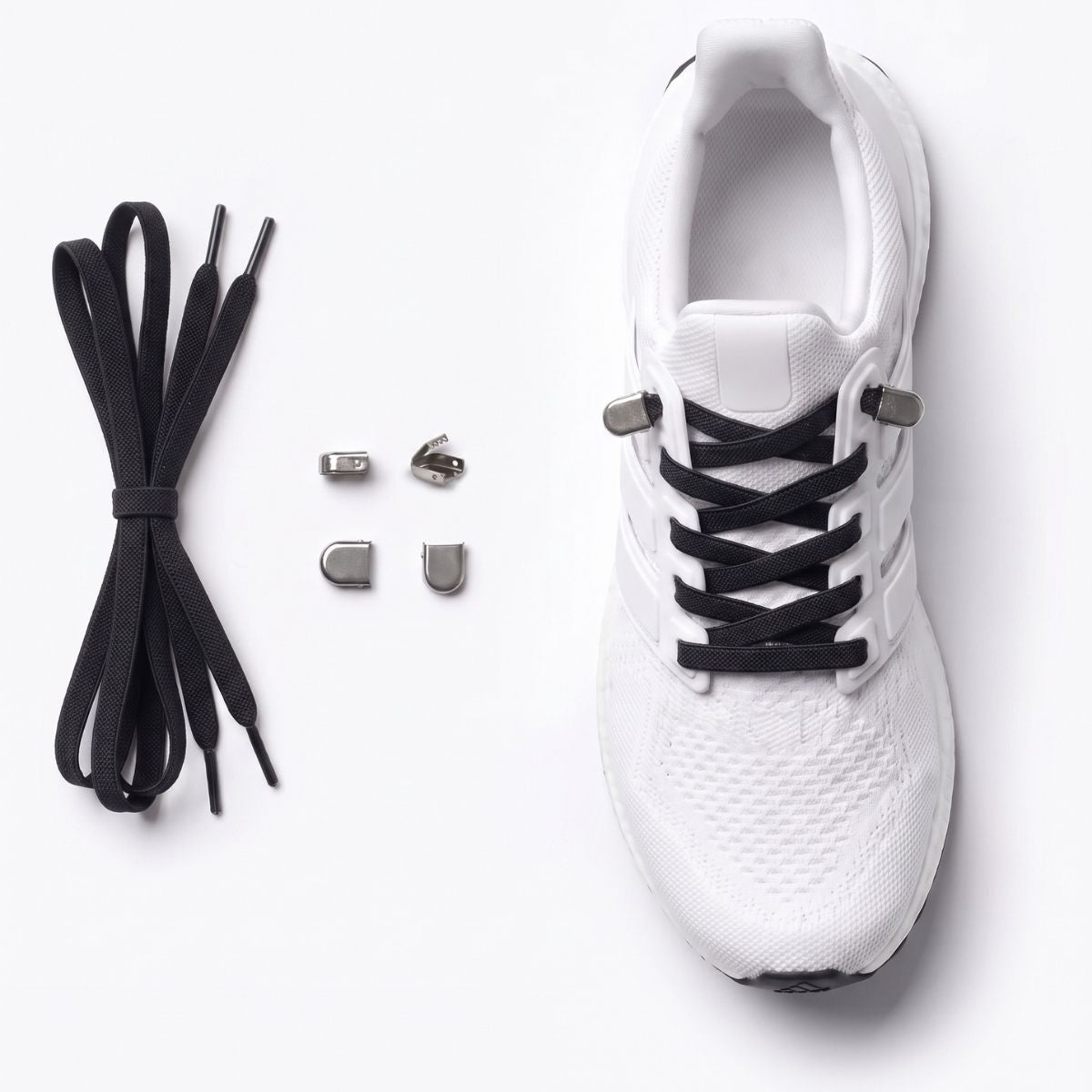 White athletic shoe with black no-tie shoelaces and small silver metal buckles, shown on a clean white background with the laces and eyelets laid out beside it.
