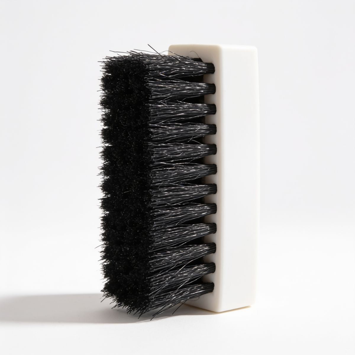 A close-up of a cleaning brush with dense black bristles and a white rectangular handle, shown against a clean white background.
